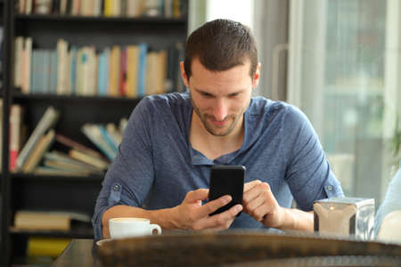 Front view portrait of a serious man checking phone content in a bar or homeの写真素材
