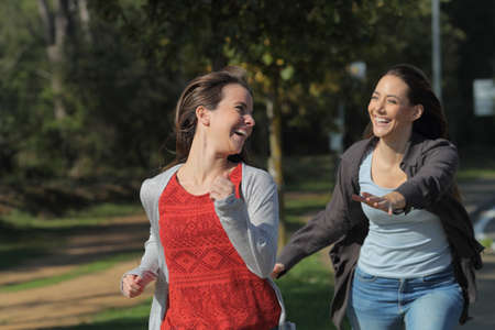 Two happy friends joking chasing running towards camera in a parkの写真素材