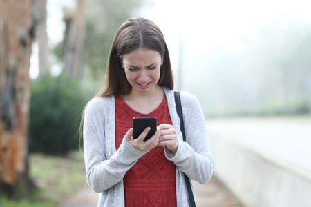 Front view portrait of an sad woman crying walking using mobile phone in a parkの写真素材