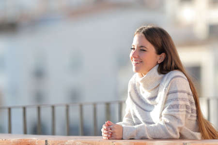 Happy girl with sweater looks away in a balcony a sunny day in winterの写真素材