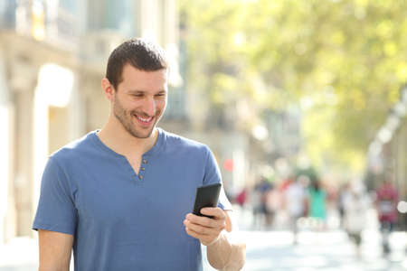 Happy man walking using mobile phone walking in the street of a big cityの写真素材