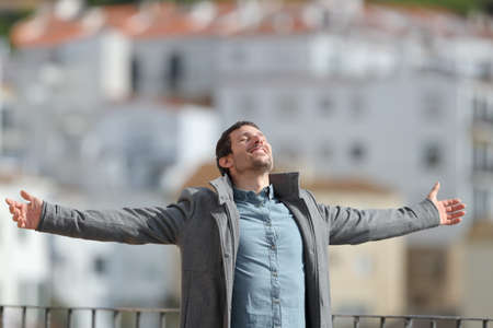 Happy man wearing jacket celebrating new day stretching arms in winter in a rural townの写真素材