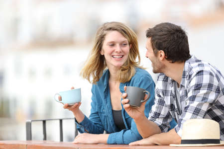 Happy adult couple talking and drinking coffee standing outdoors in a balcony in a rural townの写真素材
