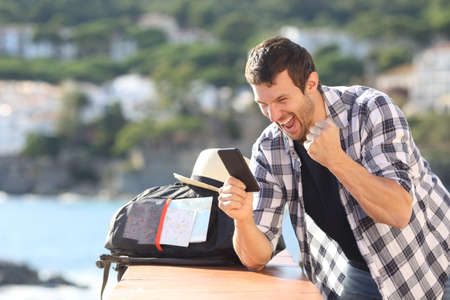 Excited tourist checking mobile phone good news in a coast town on summer vacationの写真素材