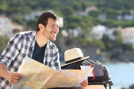 Happy tourist holding map contemplating views from a balcony on summer vacation on the beachの写真素材