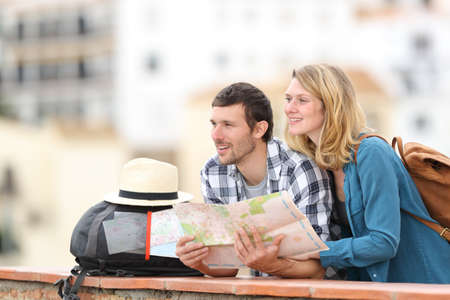 Happy couple of tourists sightseeing holding paper map standing outdoors in a balcony in a rural townの写真素材