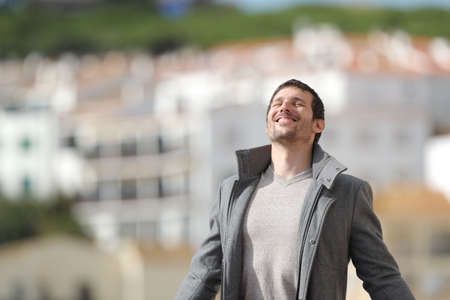 Happy adult man wearing jacket breaths deeply fresh air standing in a town in winterの写真素材