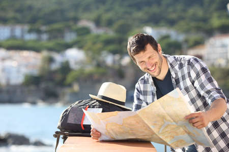 Happy tourist checking map traveling in a coast town on summer vacationの写真素材