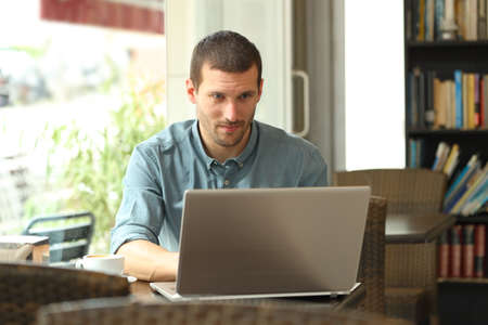 Serious man typing on laptop entering data sitting in a coffee shopの写真素材