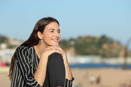 Happy casual girl contemplating views sitting outdoors on the beach a sunny dayの写真素材