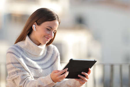 Satisfied woman e-learning using tablet and wireless earphones in a balcony in winterの写真素材