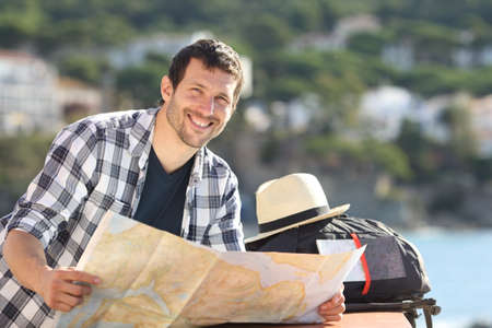 Happy tourist holding map looks at camera in a coast town on summer vacationの写真素材