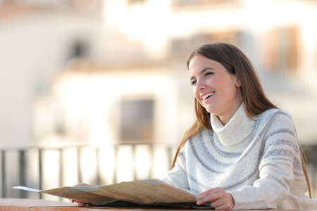 Happy tourist holding paper map looking away in a balcony on winter vacationの写真素材