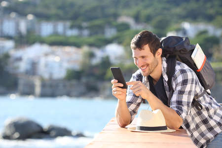 Happy tourist checking mobile phone in a balcony in a coast town on summer vacationの写真素材