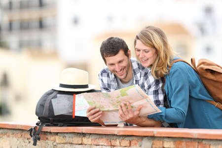 Happy couple of tourists checking map on vacation standing outdoors in a balcony in a rural townの写真素材