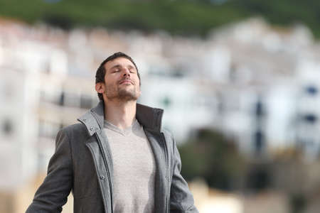 Adult man wearing jacket breaths deeply fresh air standing in a rural town in winterの写真素材