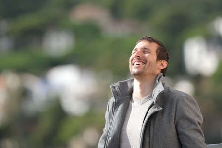 Happy adult man wearing jacket breathing fresh air outdoors in winter in the mountainの写真素材