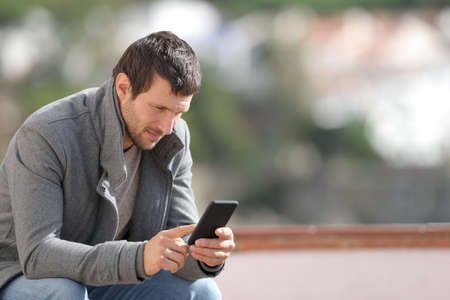 Serious adult man using smart phone in winter sitting outdoors in a townの写真素材