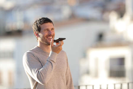 Adult man using voice recognition on mobile phone walking in a town a sunny dayの写真素材