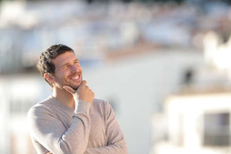 Happy pensive adult man looking at side standing in a town a sunny dayの写真素材