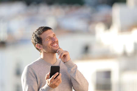 Man wondering holding smart phone looking at side standing outdoors in a rural townの写真素材