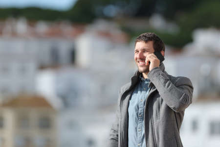 Happy man in winter talking on phone standing outdoors in a rural townの写真素材