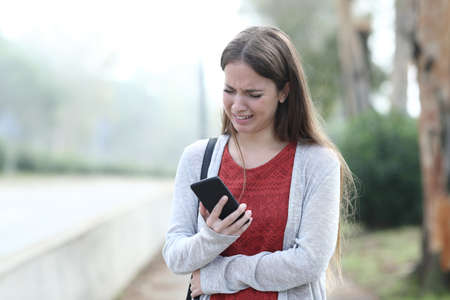 Front view portrait of a sad woman complaining and crying holding phone a foggy dayの写真素材