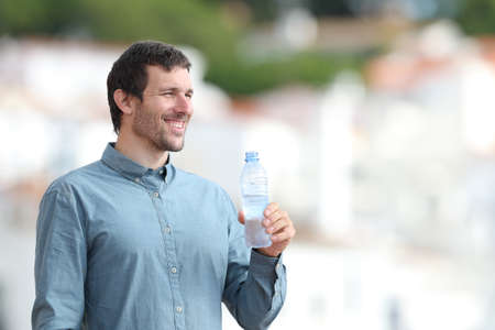 Happy adult man holding a bottle of water standing outdoors in a rural townの写真素材