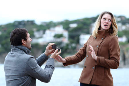 Shocked girlfriend rejecting marriage proposal of a sad man on the beach in winter