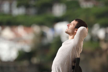 Side view portrait of a happy man relaxing sitting on a bench in a town a sunny dayの写真素材