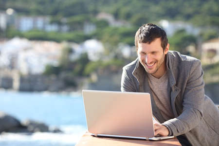 Happy man using a laptop in a balcony in winter on the beachの写真素材