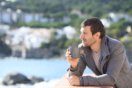 Serious man drinking coffee contemplating views in winter in a balcony on the beachの写真素材
