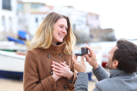 Man proposing marriage and happy girlfriend accepting in winter holiday on the beachの写真素材