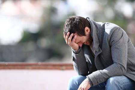 Worried man complaining alone sitting on a bench in winter in a townの写真素材