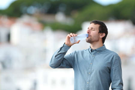 Adult casual man drinking bottled water standing outdoors in a rural townの写真素材