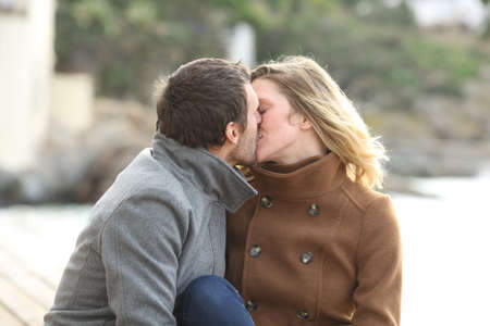 Adult romantic couple in love kissing sitting on the beach in winterの写真素材