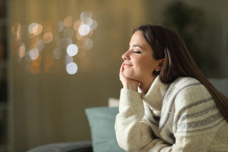 Relaxed woman meditating sitting on a couch in the living room at home in the night in winterの写真素材