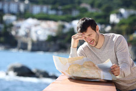 Worried lost tourist checking paper map on vacation in a coast townの写真素材