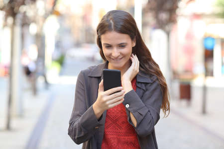 Front view portrait of a candid teen checking smart phone text walking in the streetの写真素材