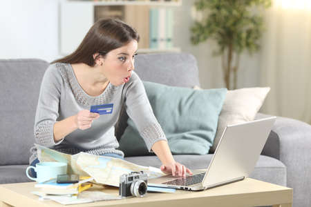 Amazed tourist paying on-line with credit card planning vacation sitting on a couch in the living room at homeの写真素材