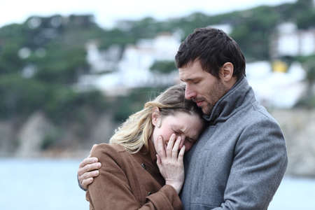 Worried man comforting a sad woman in winter on the beachの写真素材