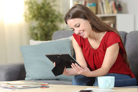 Happy woman remembering looking at photo frame sitting on a couch in the living room at homeの写真素材