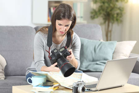 Confused tourist trying to set a complicated dslr camera sitting on a couch in the living room at homeの写真素材