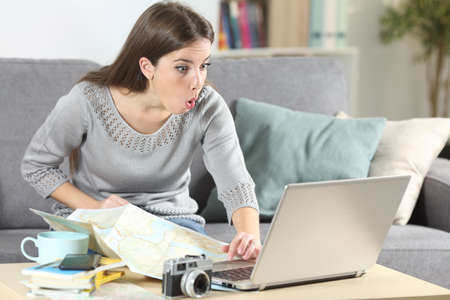 Surprised tourist planning vacation checking laptop sitting on a couch in the living room at homeの写真素材