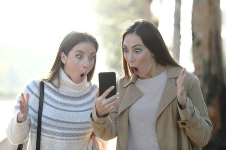 Front view portrait of a surprised women checking phone in a foggy parkの写真素材