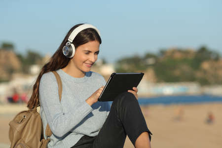 Happy girl e-learning using tablet and headphones sitting in a coast town a sunny dayの写真素材