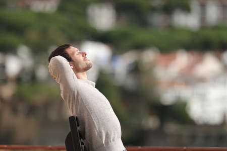Profile of a relaxed man sitting on a bench outdoors in a town in a sunny day