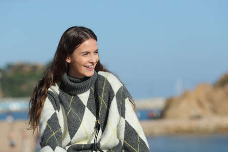Happy girl wearing sweater contemplating views sitting in a coast town beachの写真素材