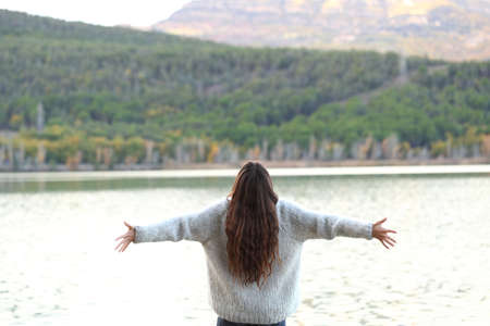 Back view of happy woman celebrating holidays outstretching arms in a lake