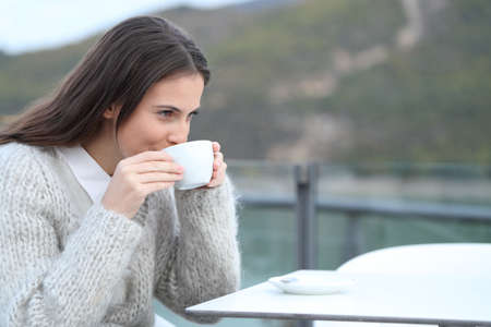 Happy girl drinking hot coffee sitting in a restaurant terrace in the mountain